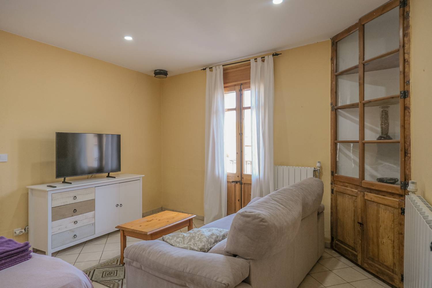 Saló lluminós de l’apartament a Sant Jaume de Llierca amb sofà, taula de menjador i vistes a la plaça.